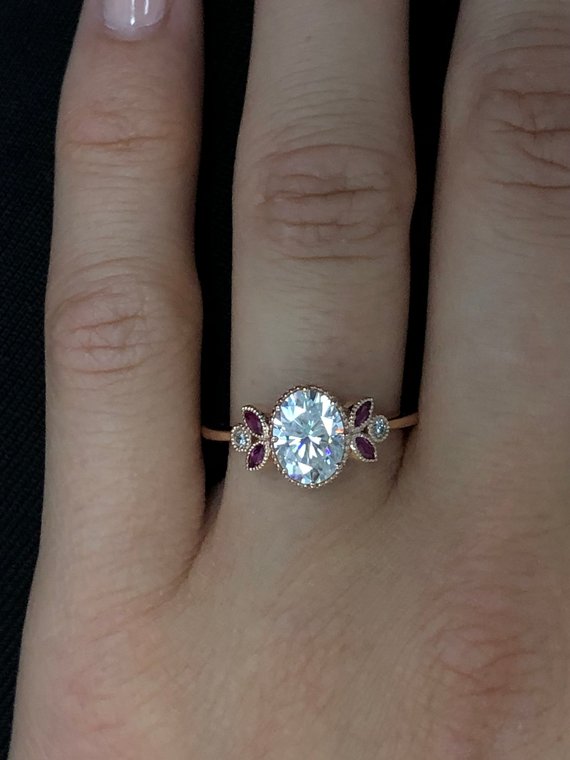 Oval engagement ring with marquise rubies in rose gold in a hand